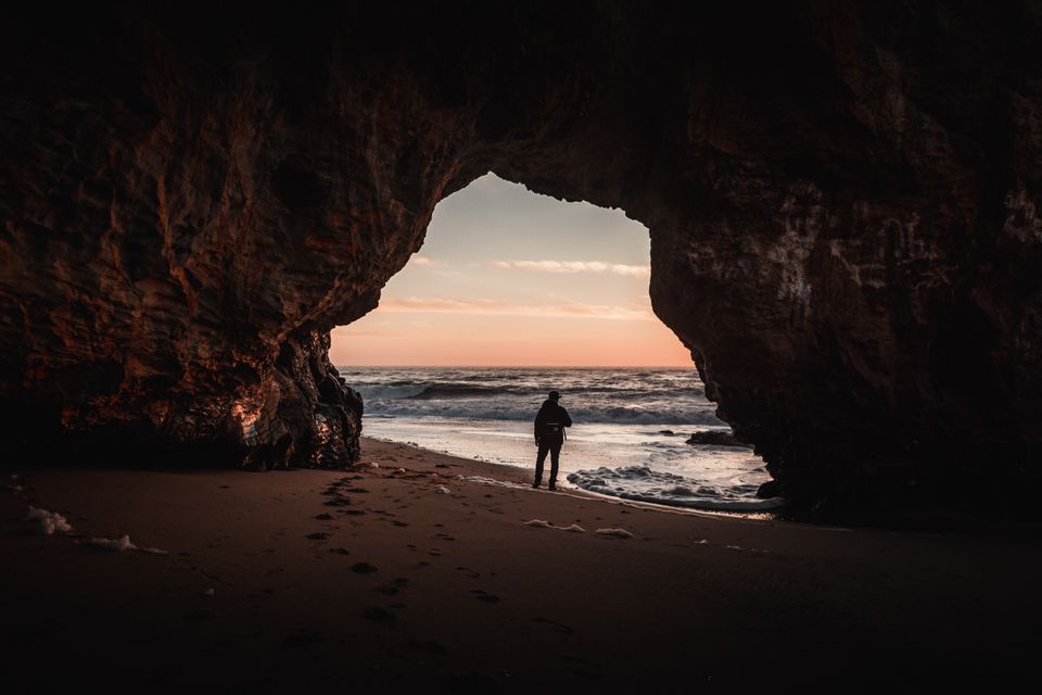 Man by a beach cave opening representing a sanctuary 
