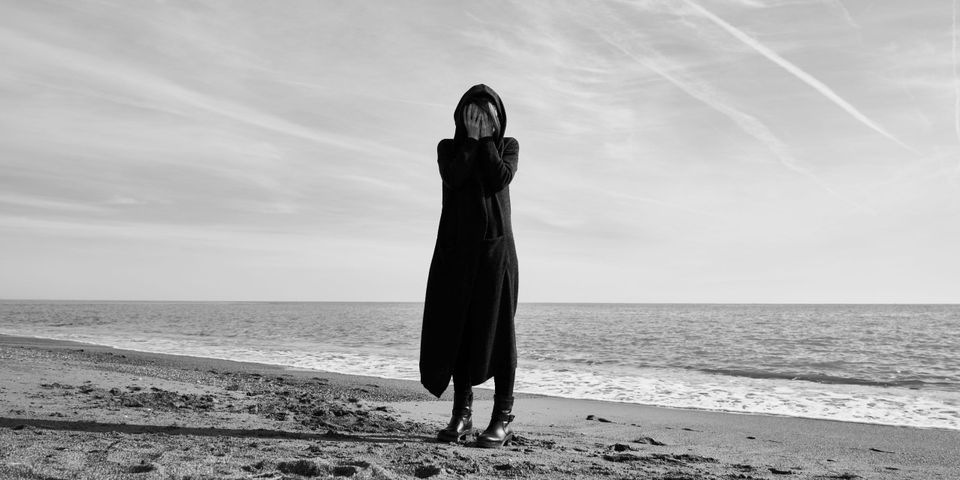 woman on a beach covering her face representing an existential crisis