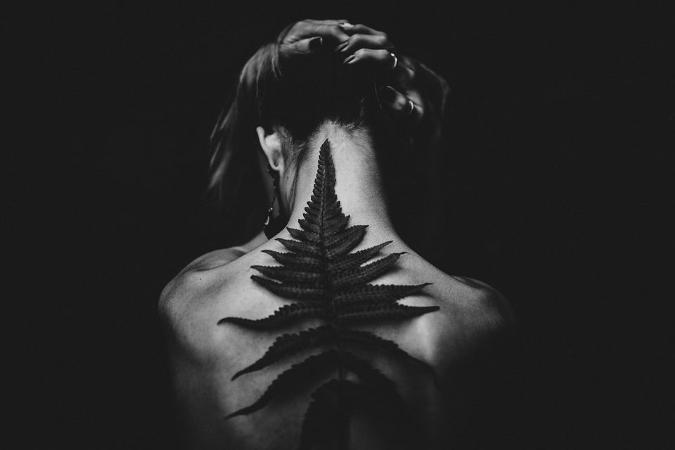 A black and white image of a woman with a leaf on her back (representing face your pain)
