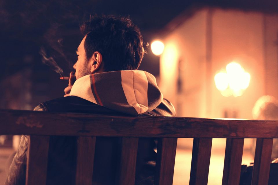 Man on a bench smoking representing feeling like you don't belong